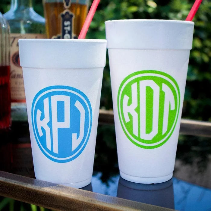 Two white foam cups with personalized monogrammed initials on them, placed on a table with a red straw visible.