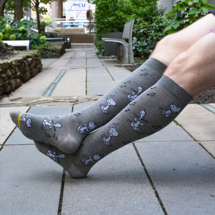 Grey heather knee-high compression socks for men with a dancing Snoopy design, worn in a lifestyle setting.