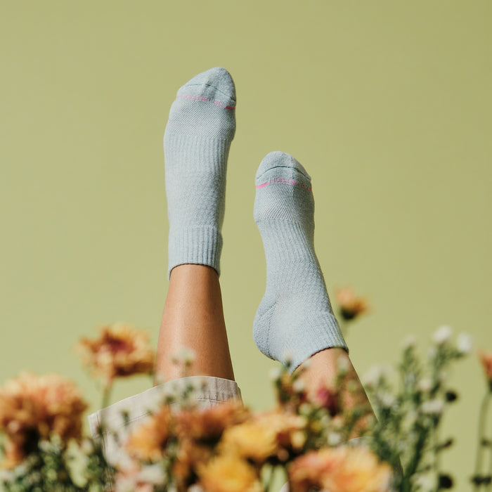 Light blue quarter compression socks with ribbed cuffs, displayed against a green background and surrounded by flowers.
